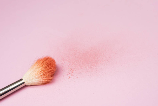 Makeup brush next to the texture of scattered colored face powder. A brush made of goat hair lies against the background of a broken blush. - Фото, изображение