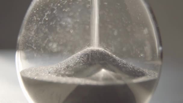 Close-up van het onderste deel van de zandloper met naar beneden vallend grijs zand. Transparante zandglasmeettijd. Concept van levensmeting, seconden, timing. - Video