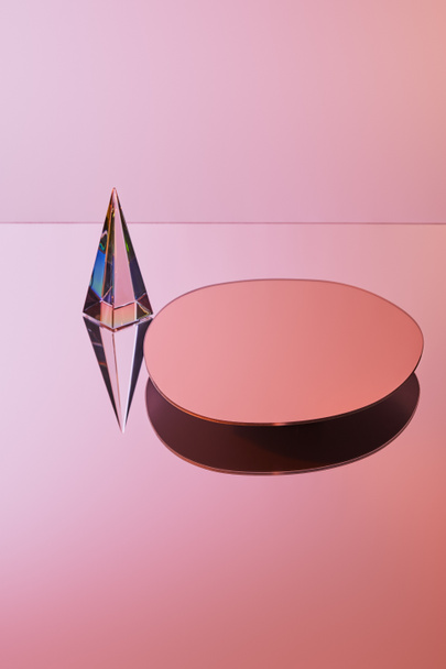 crystal transparent pyramid with reflection near round mirror on pink background - Photo, Image