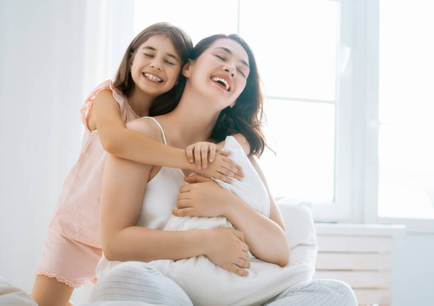 A nice girl and her mother enjoy sunny morning. Good time at home. Child wakes up from sleep. Family playing on the bed in the bedroom. - Фото, зображення