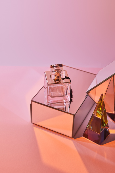 crystal transparent pyramid near perfume bottle and mirror cubes on pink background - Foto, Imagem