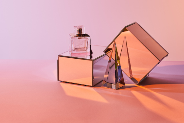 pirámide transparente de cristal cerca de botella de perfume y cubos de espejo sobre fondo rosa
 - Foto, imagen