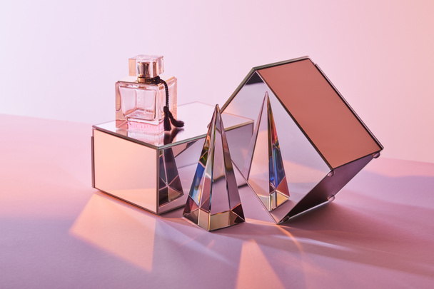 crystal transparent pyramid near perfume bottle and mirror cubes on pink background - Photo, Image