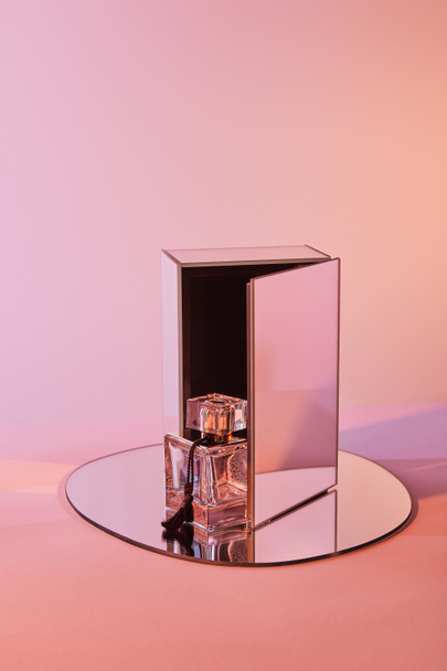 parfum fles op ronde spiegel met kubus op roze achtergrond - Foto, afbeelding