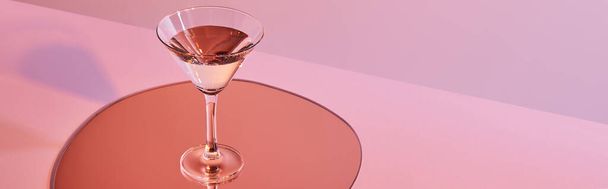 cocktail glass with liquid on mirror with reflection on pink background, panoramic crop - Foto, immagini