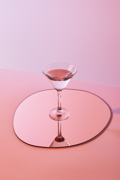 cocktail glass with liquid on mirror with reflection on pink background - Fotoğraf, Görsel