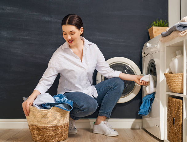 Beautiful young woman is smiling while doing laundry at home.                                  - Foto, Imagem