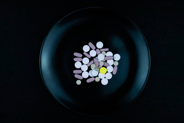 Black plate full of pills one yellow with smile icon - Photo, Image