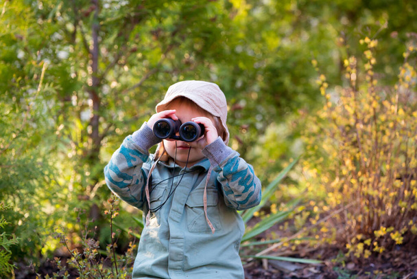 Blonde little toddler child with binoculars, sitting in garden on sunset, playing - Photo, Image