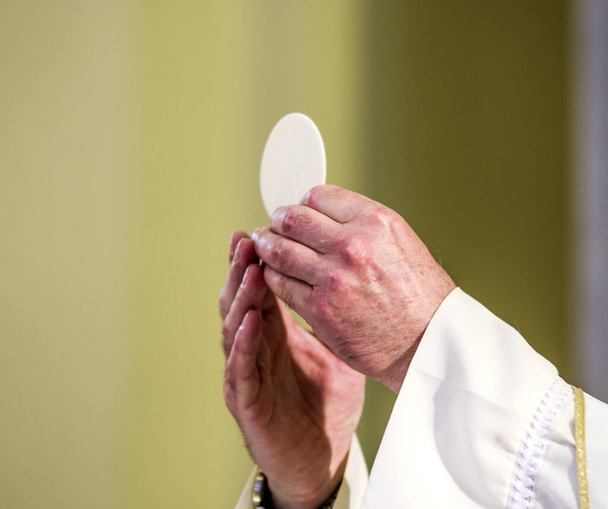Während der Messfeier weihen die Hände des Priesters, wie die Hände von Papst Franziskus, die Hostie, die zum Leib Christi wird - Foto, Bild