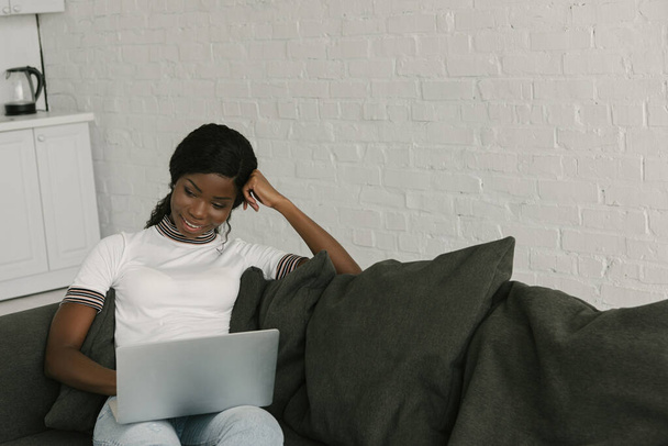 アフリカ系アメリカ人のフリーランスがソファに座ってノートパソコンを使って  - 写真・画像