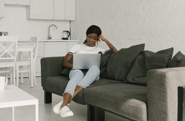 koncentrált afro-amerikai szabadúszó dolgozik laptop kanapén a konyhában - Fotó, kép