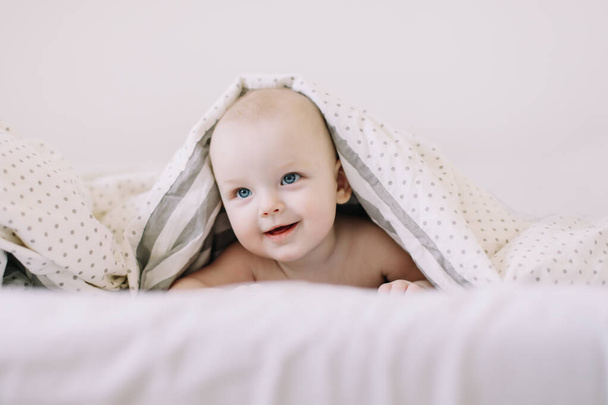 Adorable baby learning to crawl in white  bedroom. Cute funny baby lying under the blanket on bed. Little child doing tummy time - Foto, Imagem