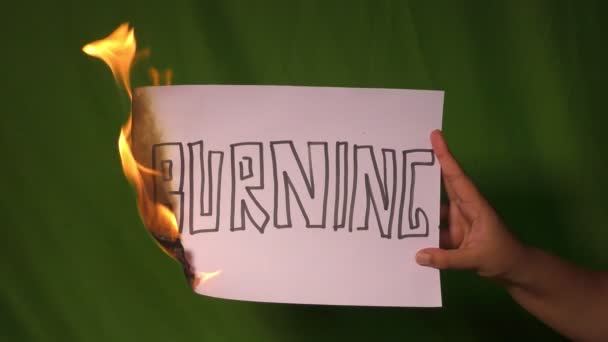 Een hand houdt het brandende papier met brandende tekst woord op het groene scherm achter. - Video