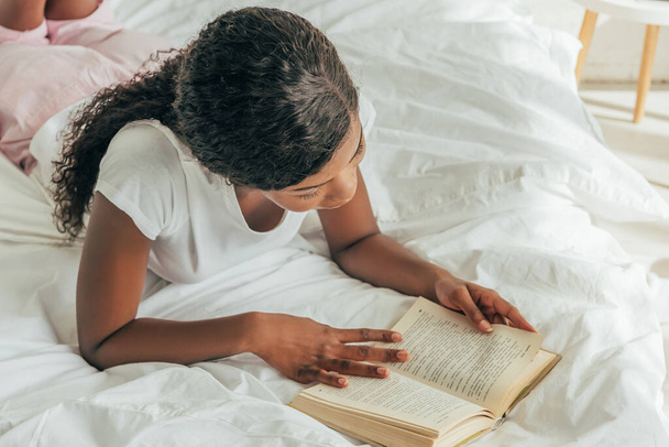 γενικά άποψη της νεαρής Αφροαμερικανής γυναίκα ανάγνωση βιβλίο στο κρεβάτι - Φωτογραφία, εικόνα
