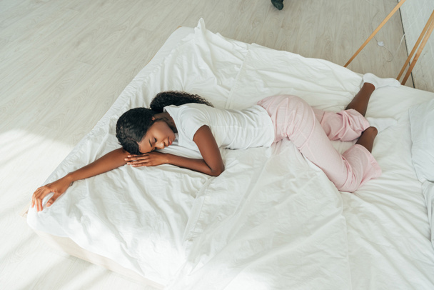 korkea kulma näkymä afrikkalainen amerikkalainen tyttö pyjama nukkuu valkoinen vuodevaatteet
 - Valokuva, kuva