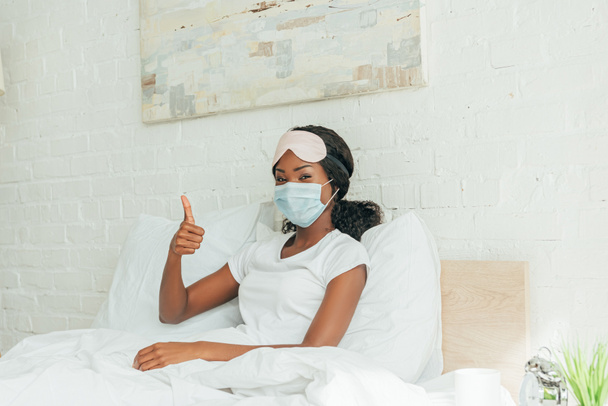 menina americana africana em máscara médica mostrando polegar para cima enquanto olha para a câmera
  - Foto, Imagem