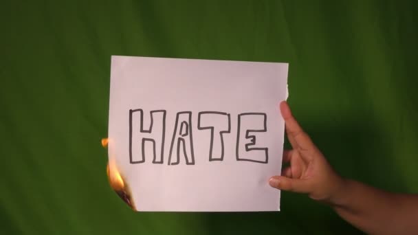 Ręka trzyma płonący papier z tekstem nienawiści na nim na zielonym ekranie za. - Materiał filmowy, wideo