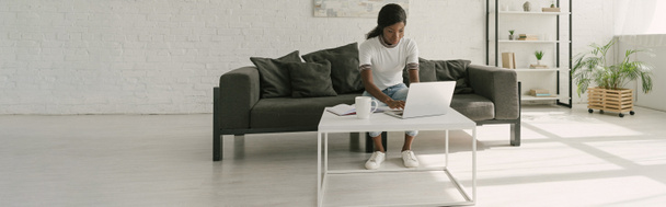 immagine orizzontale di freelance afro-americano che lavora su laptop in un ampio soggiorno
 - Foto, immagini