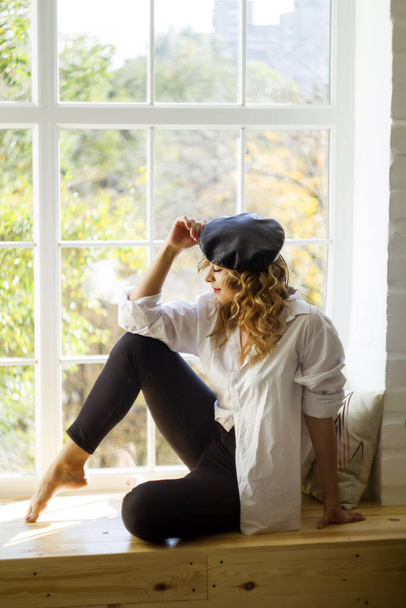 Young beautiful woman sitting at daylight on windowsill looking outside - Фото, зображення