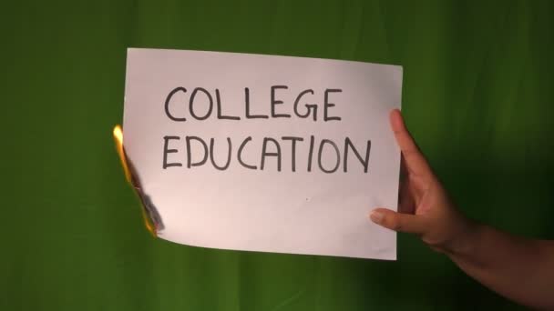 Una mano tiene la carta in fiamme con la parola di testo di istruzione universitaria su di esso sullo schermo verde dietro
. - Filmati, video
