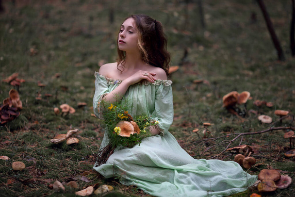 παραμύθι για μια νεράιδα σε ένα μαγικό δάσος, ένα όμορφο κορίτσι σε ένα πράσινο φόρεμα βόλτες στο δάσος με ένα μπουκέτο, μανιτάρια σε ένα μπουκέτο - Φωτογραφία, εικόνα
