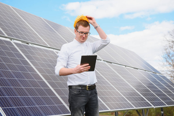 Portret mężczyzny z tabliczką w rękach stojącego w pobliżu stacji paneli słonecznych. Ekologiczne wytwarzanie energii. Koncepcja rozwoju stacji słonecznej. Budowa domu. - Zdjęcie, obraz