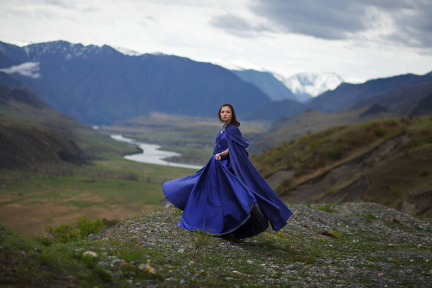 Uma menina em um vestido azul magnífico caminha nas montanhas
. - Foto, Imagem