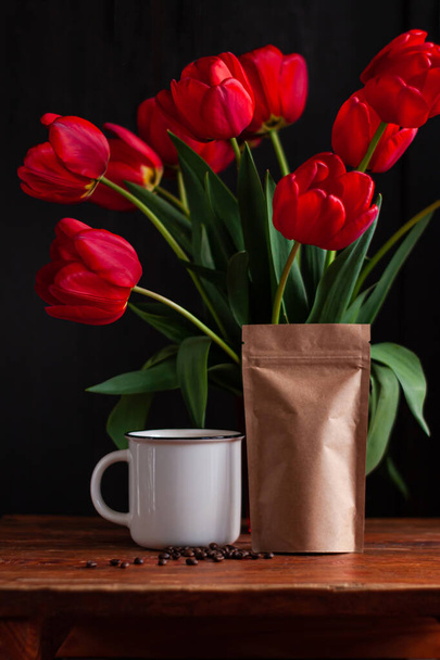 Biały kubek kawy z niesamowicie kwitnących czerwonych tulipanów bukiet na czarnym tle. Ciemny nastrój niski klucz minimalizm stylu kwiaty i gorący kubek zdjęcie baner. Stylowe miejsce do kopiowania kartki z życzeniami. Dzień dobry - Zdjęcie, obraz