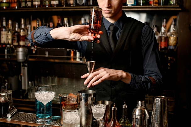 bartender holds in hand steel jigger and pours drink from bottle into it. - Fotoğraf, Görsel