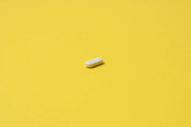 Bílá pilulka na žlutém pozadí, izolovat, s místem pro text - Fotografie, Obrázek