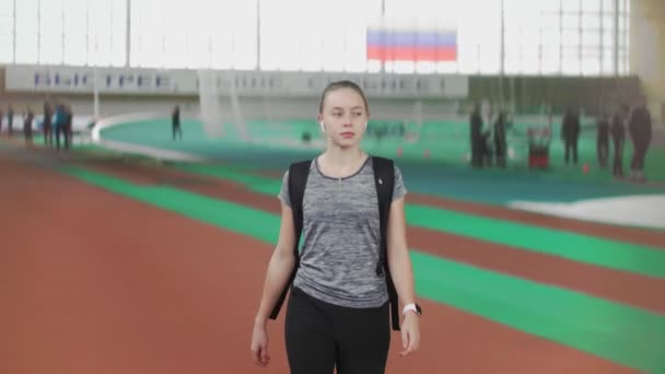 Fiatal női futó jön a sport arénába és integet a barátainak. - Felvétel, videó