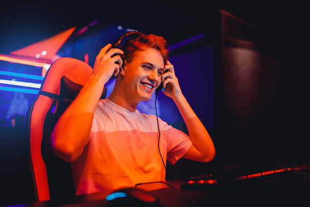 Streamer young man rejoices in victory professional gamer playing online games computer with headphones, neon color - Fotografie, Obrázek