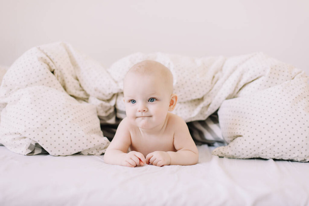 Portrait of baby hiding under the white blanket. Cute 8 month baby girl crawling in bed. Tummy Time. Textile and bedding for kids - Photo, Image