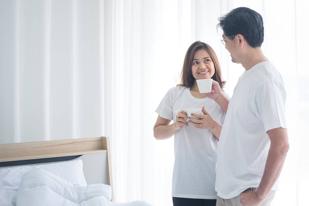 A senior Asian couple is drinking coffee at home. They smiled happily and were talking in the bedroom. This was distance from society. - Foto, Imagem