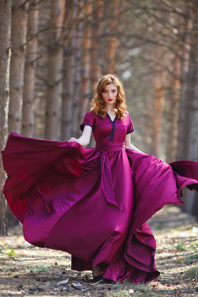 vörös hajú lány egy burgundi ruhában sétál az erdőben. - Fotó, kép
