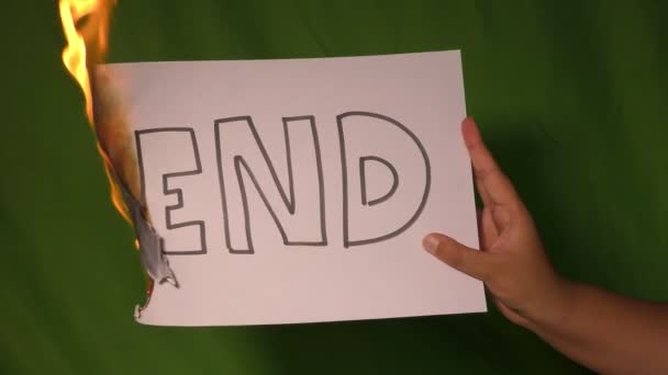 Een hand houdt het brandende papier met eindtekst woord op het groene scherm achter. - Video
