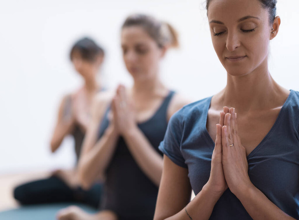 ヨガとマインドフルネス瞑想を一緒に練習している女性たちは、手を握りしめ、リラックスし、健康的なライフスタイルと精神性の概念 - 写真・画像