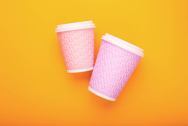 Par de copos de café de papelão rosa em um fundo amarelo
 - Foto, Imagem
