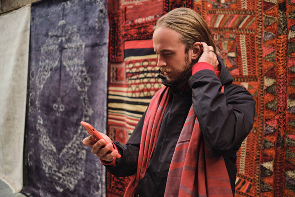 Nuori houkutteleva mies käyttää älypuhelinta kävellessään paikallisten turkkilaisten markkinoilla
 - Valokuva, kuva