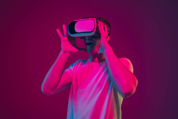 Caucasian mans portrait isolated on pink-purple studio background in neon light, playing with VR-headset - Foto, afbeelding
