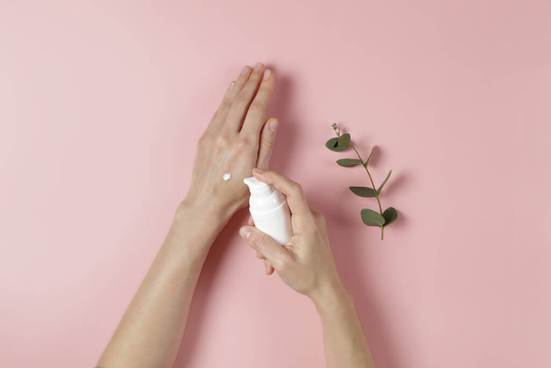 Revitalizing hand cream for healing and recovery after excessive use of soap and disinfectants. Young woman applying moisturizing lotion. Copy space, close up, pink background, flat lay, top view. - Photo, Image