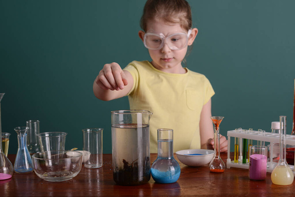 Dziewczyna w okularach bezpieczeństwa w domu robi eksperymenty z chemikaliami. eksperymenty szkolne w domu. - Zdjęcie, obraz
