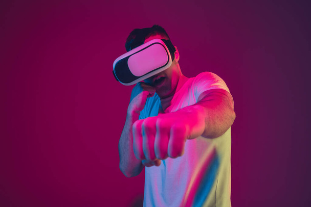 Caucasian mans portrait isolated on pink-purple studio background in neon light, playing with VR-headset - Fotoğraf, Görsel