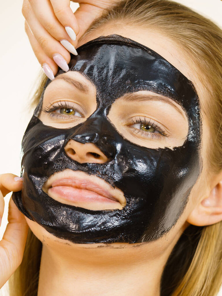 Νεαρή γυναίκα που βγάζει την μαύρη μάσκα από το πρόσωπό της, σε λευκό χρώμα. Έφηβη που φροντίζει το λιπαρό δέρμα, καθαρίζει τους πόρους. Περιποίηση ομορφιάς. Περιποίηση δέρματος. - Φωτογραφία, εικόνα