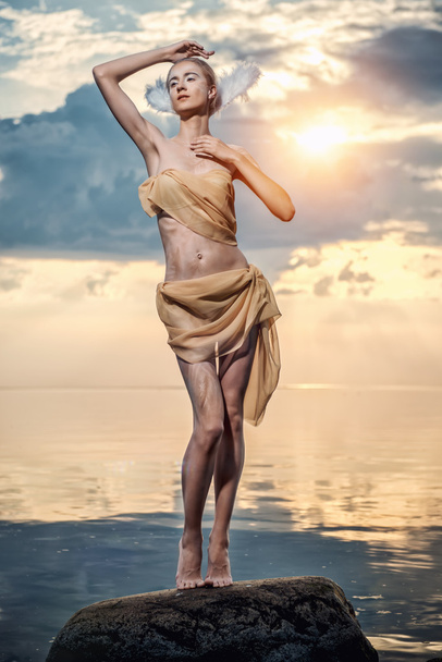 Young beautiful woman as swan posing on the beach at sunset - Foto, imagen