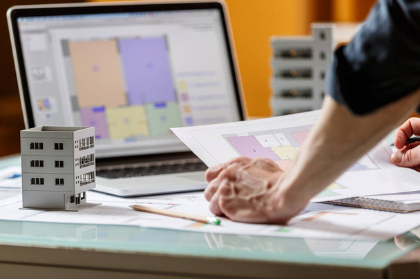 インテリアデザイナーは、設計図とラップトップをテーブルの上に置き、スタジオでアパートの計画で働いています。建築設計局作業概念 - 写真・画像