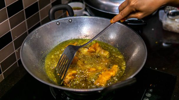 Közelkép a nyers csirkehús sült wok forró olaj a konyhában. Kézzel készített sült csirke segítségével a fém spatula. Házi készítésű étel. Forró olaj felületén lévő olajbuborékok. - Fotó, kép