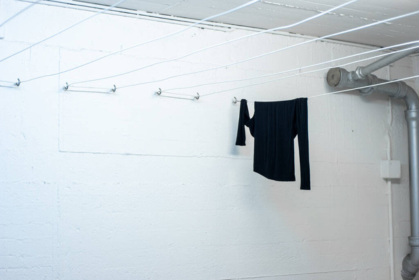 Ενιαία μαύρη μακρυμάνικη μπλούζα που κρέμεται έξω για να στεγνώσει σε μια σειρά μέσα σε μια κοινή χρήση πλυσταριό 2020 - Φωτογραφία, εικόνα
