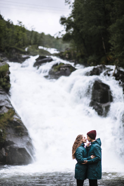 Portrait of lovers in green raincoats standing on the background of a waterfall - Foto, immagini